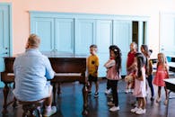 Group of children learning piano with teacher in a classroom, fostering musical education.